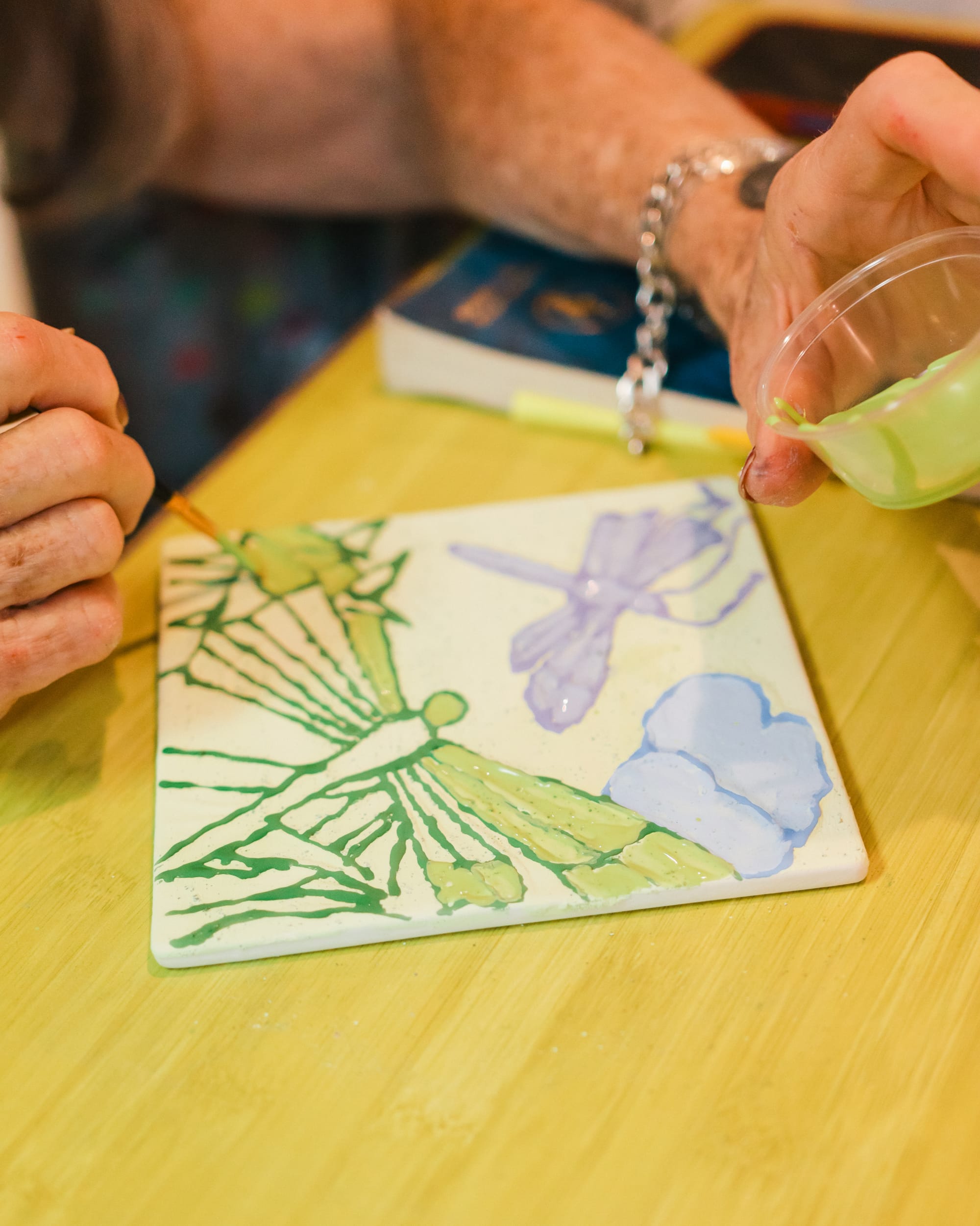 An artist carefully painting a dragonfly on pottery