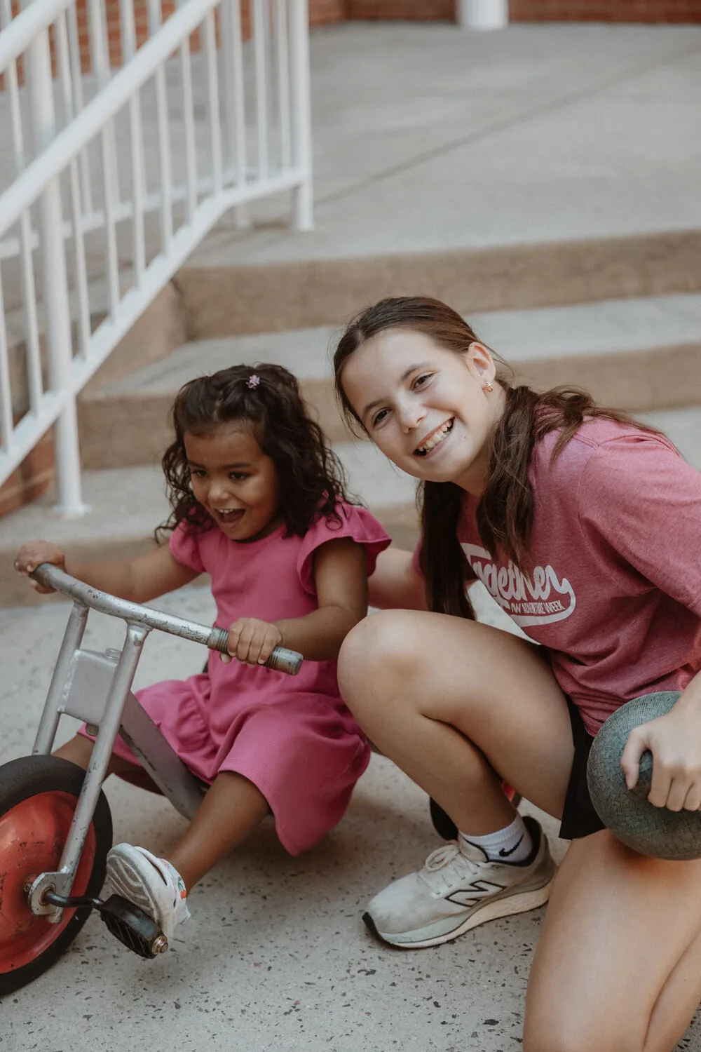 Two girls outside with a trike.
