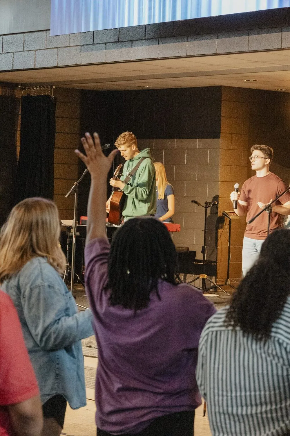Young adults singing together, hands raised.